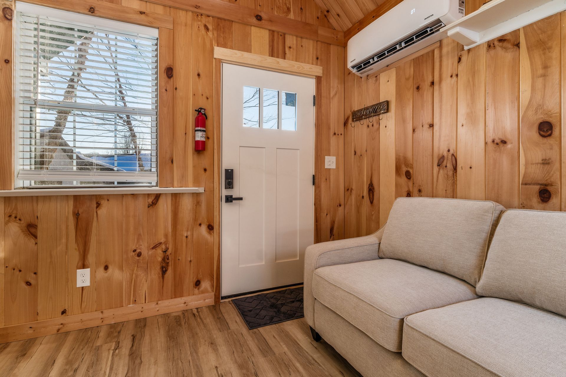 Een houten interieur met een beige bank, een witte deur en een airconditioning.
