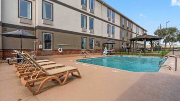 A hotel with a swimming pool, sun loungers, and a covered area.