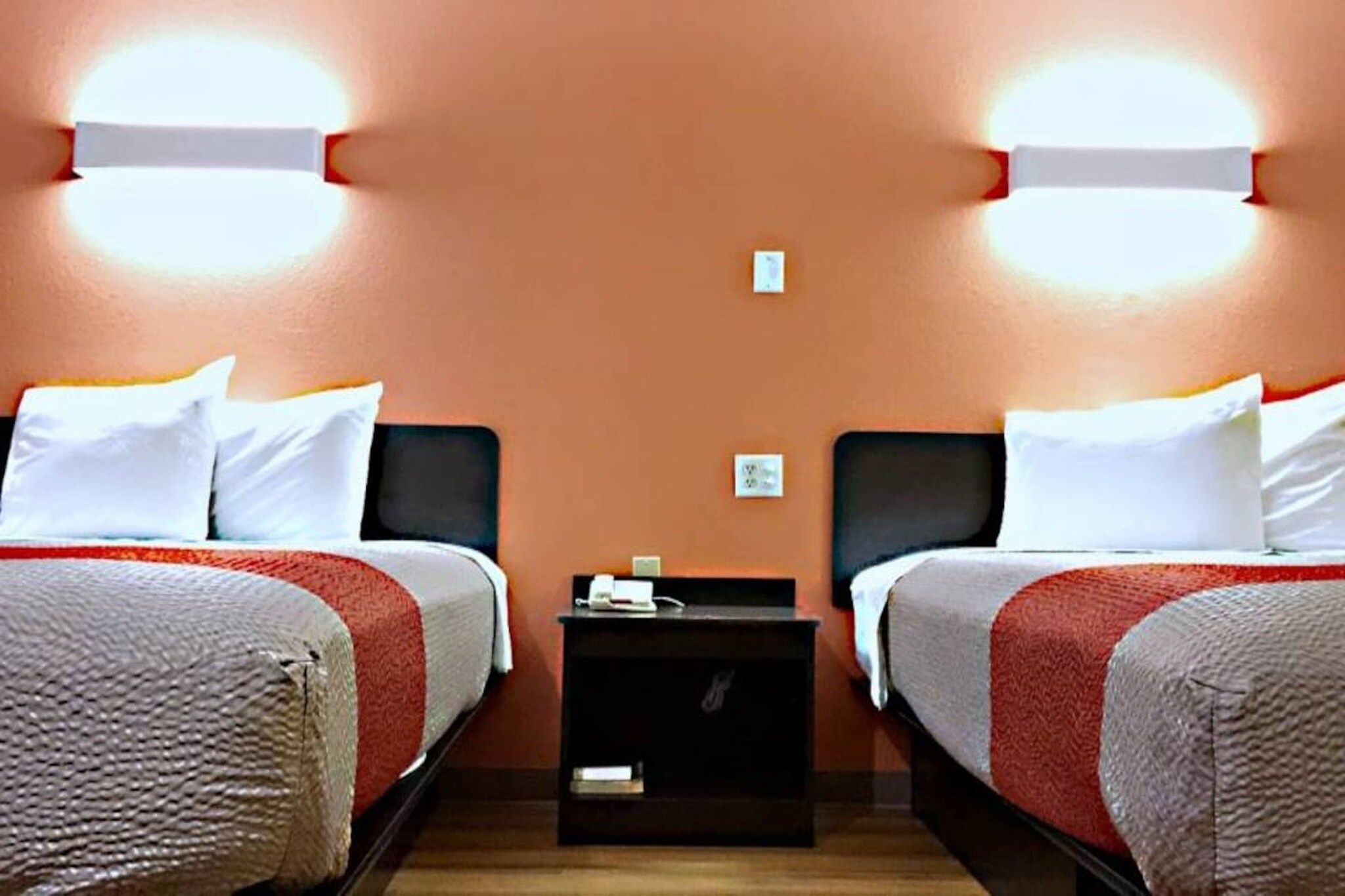 Une chambre d’hôtel avec deux lits, une table de chevet et un luminaire fixé au mur.