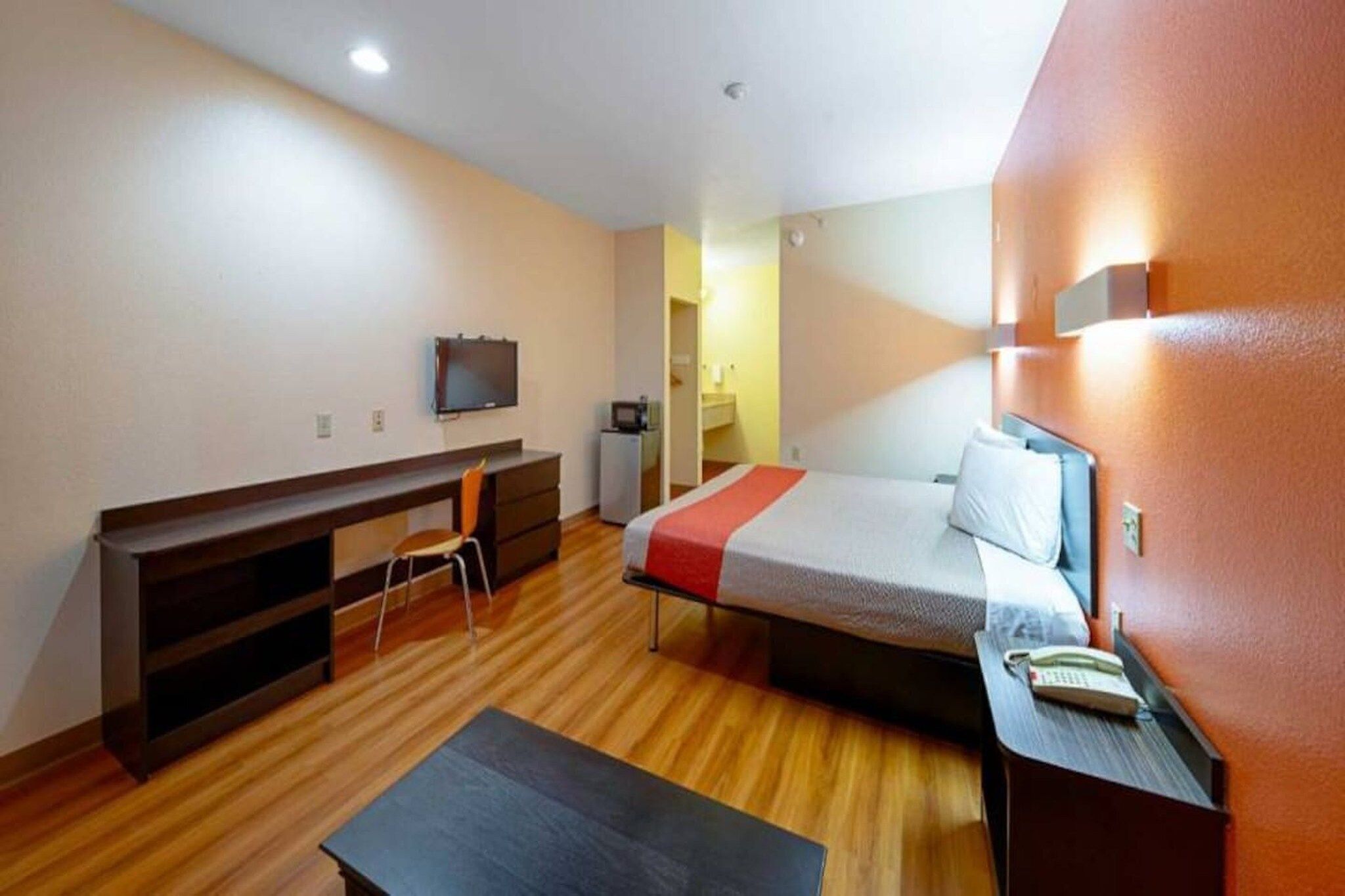 Une chambre d’hôtel de taille réduite, comprenant un lit, un bureau, une chaise, un téléviseur et une petite kitchenette.