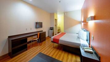 Une chambre d’hôtel de taille réduite, comprenant un lit, un bureau, une chaise, un téléviseur et une petite kitchenette.