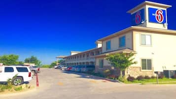 A motel with a large parking lot, multiple units, and a clear blue sky.
