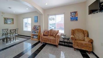 A lobby with a reception desk, two patterned sofas, a small table, and a TV mounted on the wall.