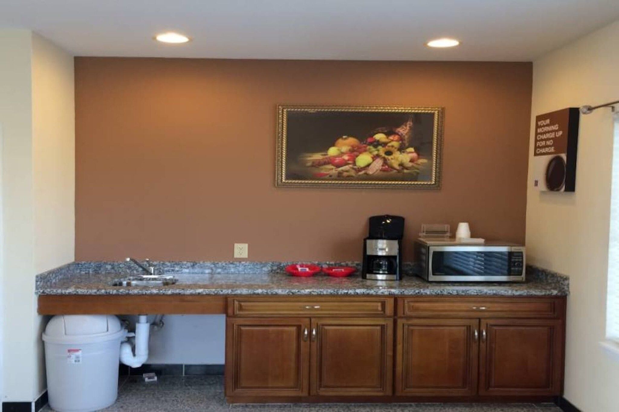 Une cuisine dotée de plans de travail en granit, de meubles en bois, d’une machine à café, d’un four à micro-ondes et d’une nature morte représentant des fruits, accrochée au mur.