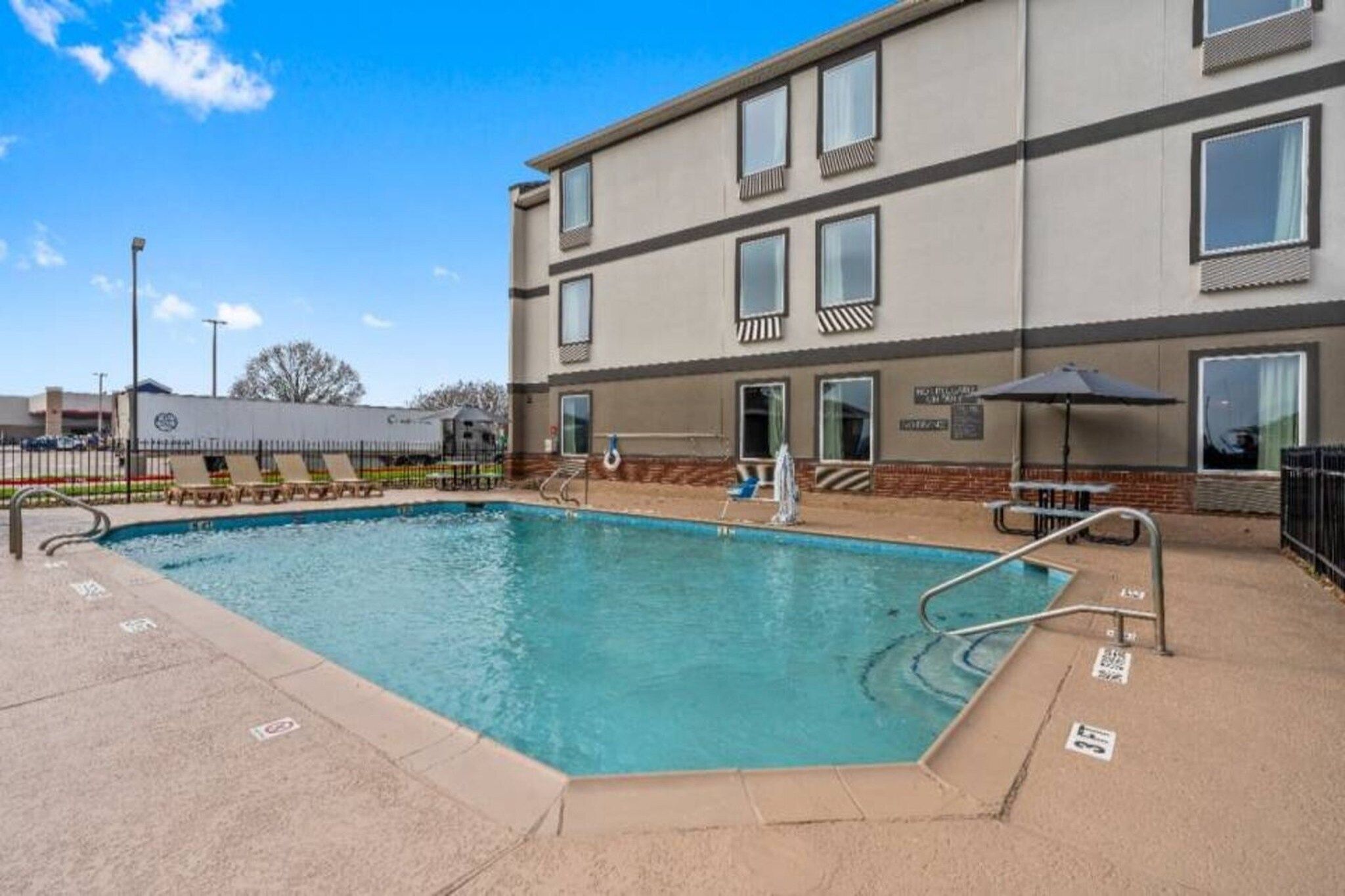 A rectangular swimming pool with a metal ladder and a few lounge chairs.