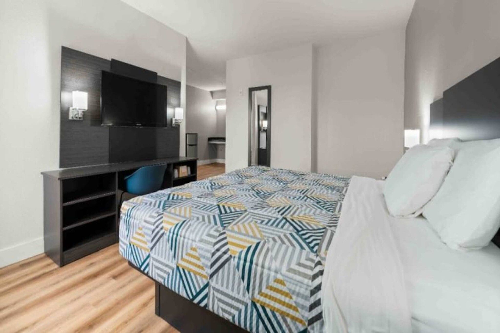 Una habitación de hotel con cama, escritorio, silla, televisor y espejo.