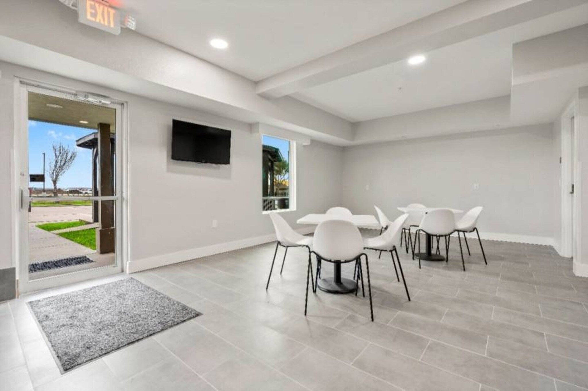 A modern interior with a conference table, chairs, a flat-screen TV, and a door leading outside.