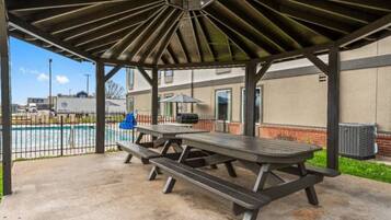 An outdoor covered picnic area with a grill and benches.