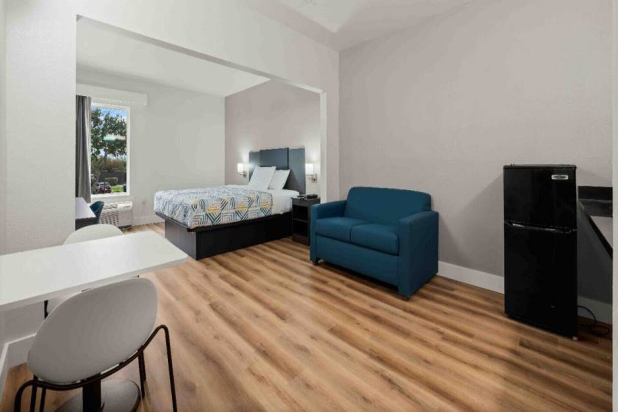 A modern room with a bed, a blue sofa, a desk, and a refrigerator.