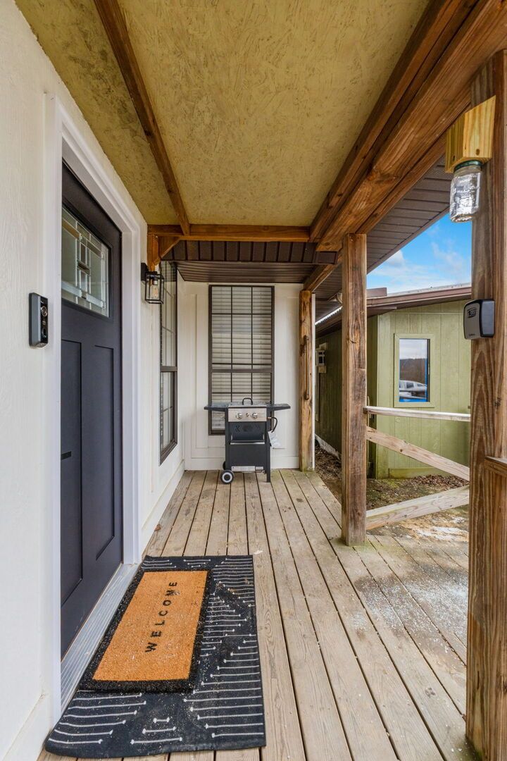 Eine Holzveranda mit Fußmatte, Grill und einer Tür mit Fenster.