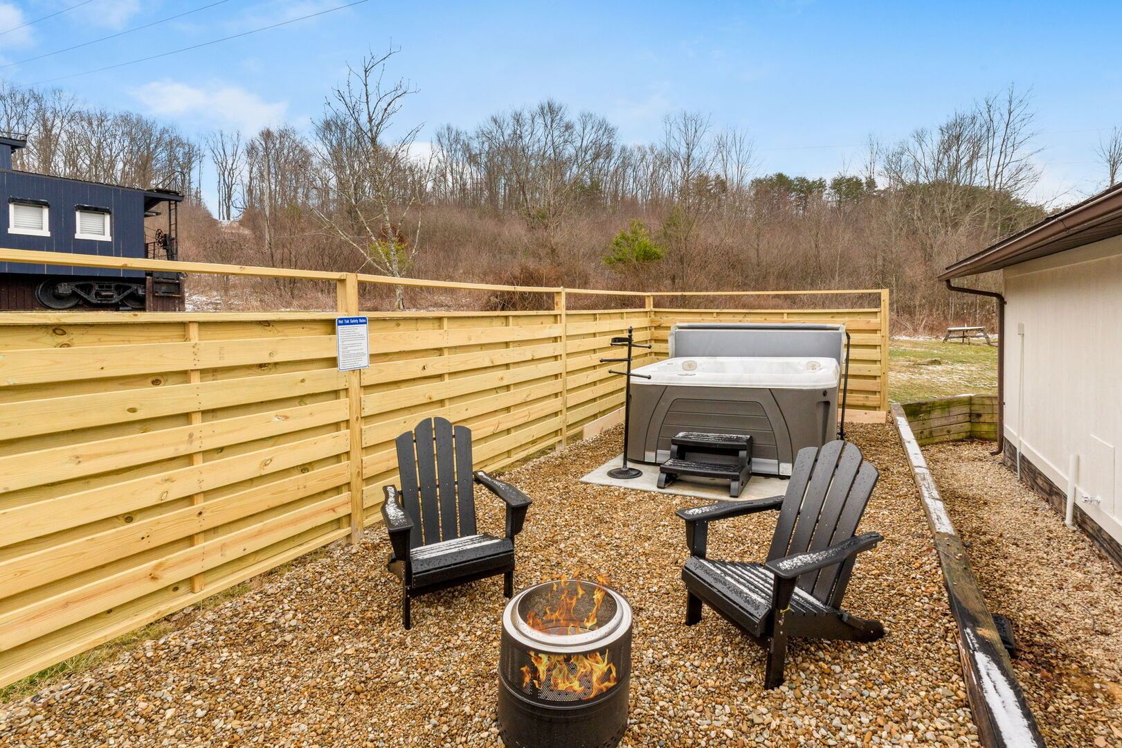 A fenced outdoor area with a hot tub, two Adirondack chairs, and a fire pit.