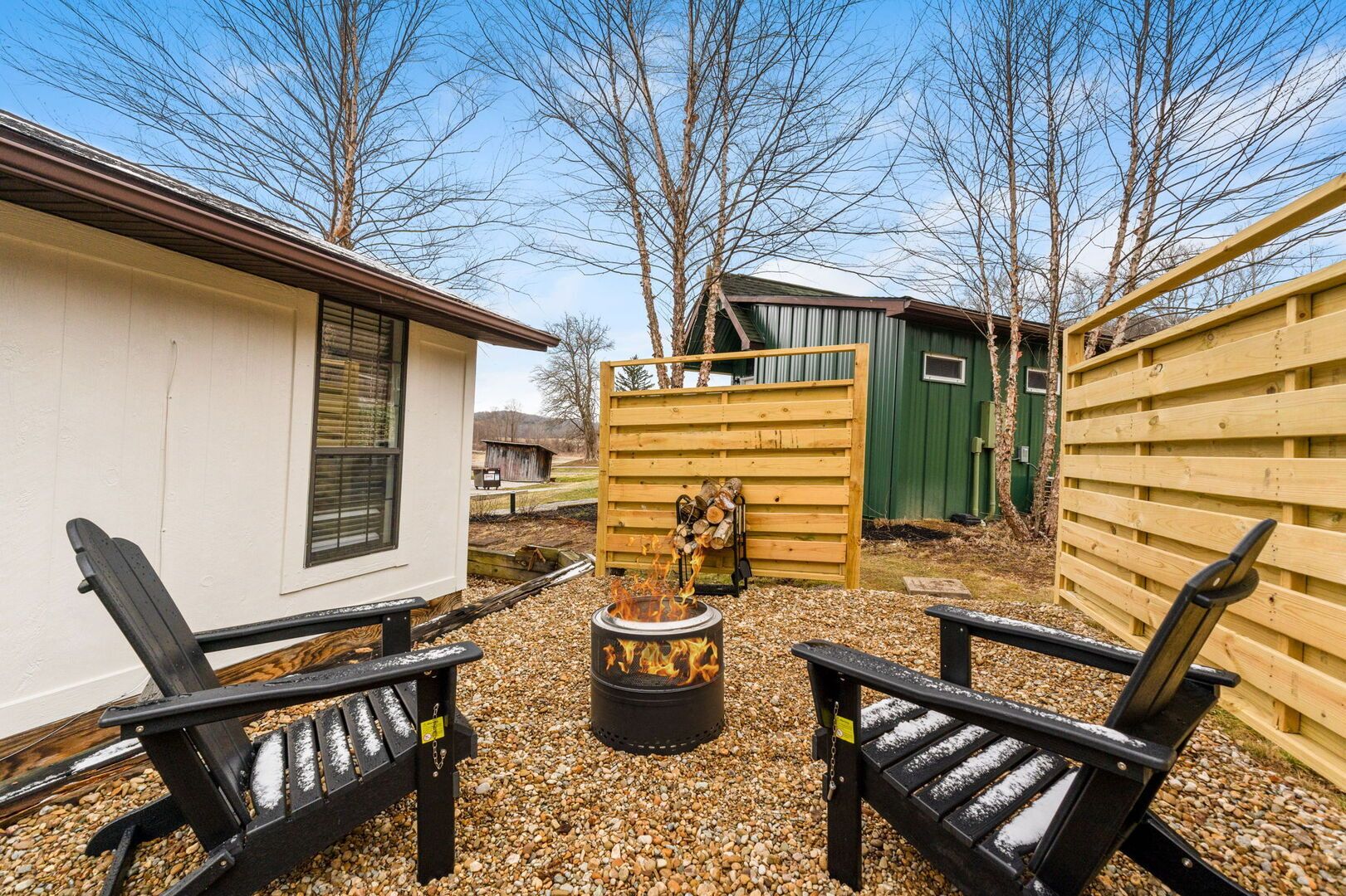 Eine Terrasse mit zwei schwarzen Stühlen, einer Feuerstelle und einem kleinen Schuppen im Hintergrund.