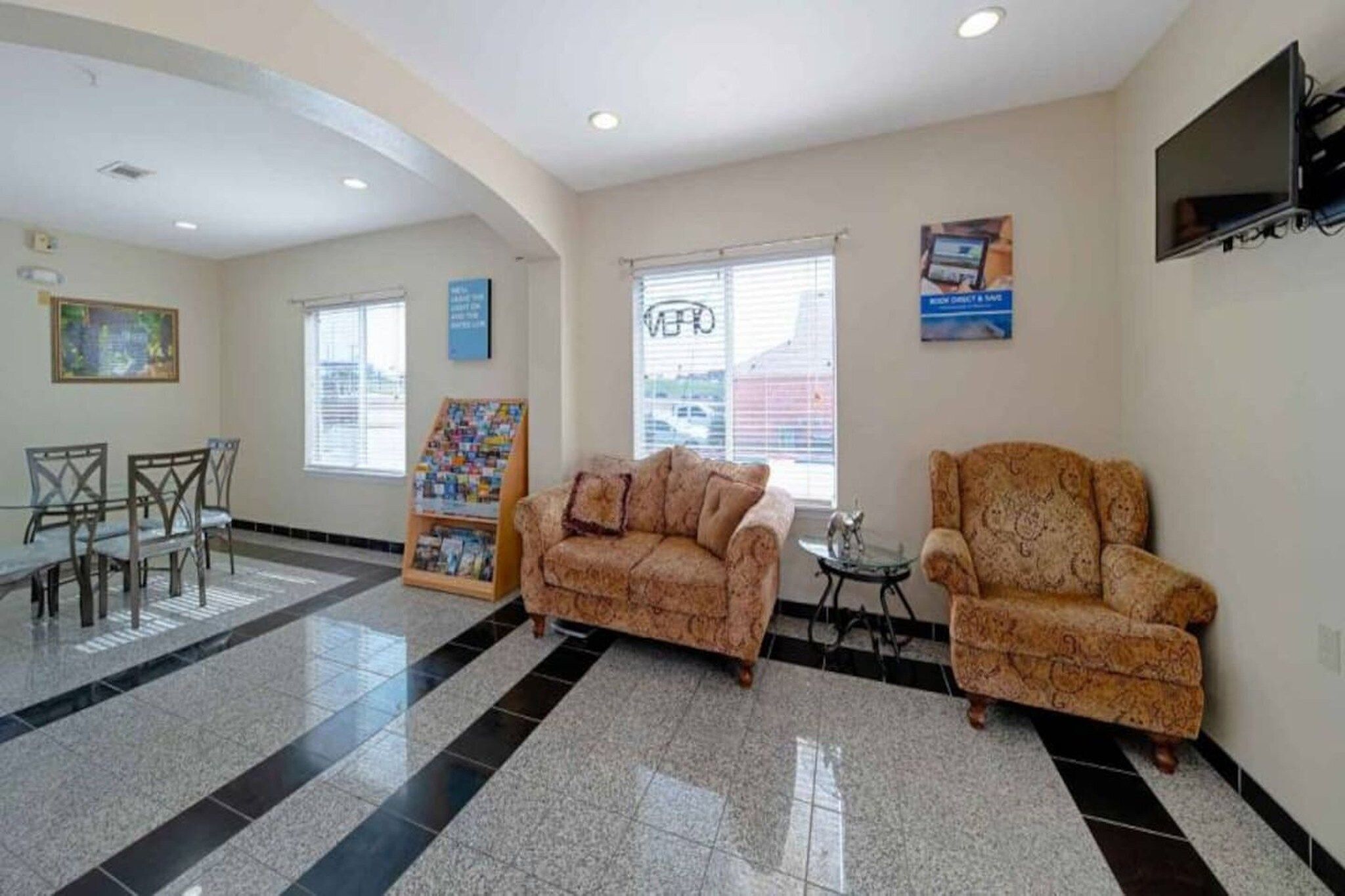 A lobby with a reception desk, two patterned sofas, a small table, and a TV mounted on the wall.