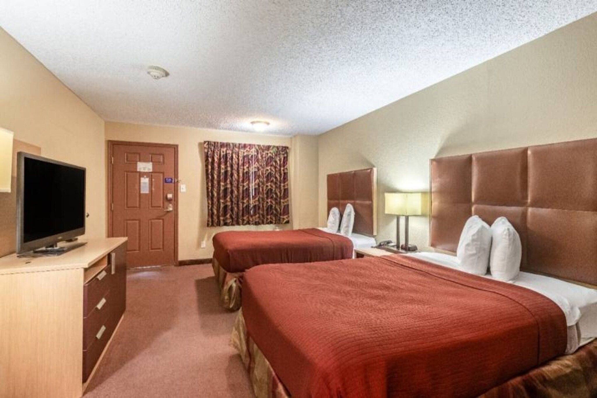 Une chambre d’hôtel avec deux lits, une télévision, un bureau et une porte.