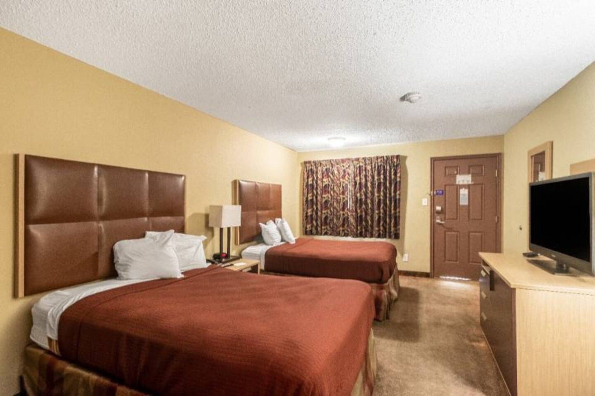 A hotel room with two beds, a television, a desk, and a door.