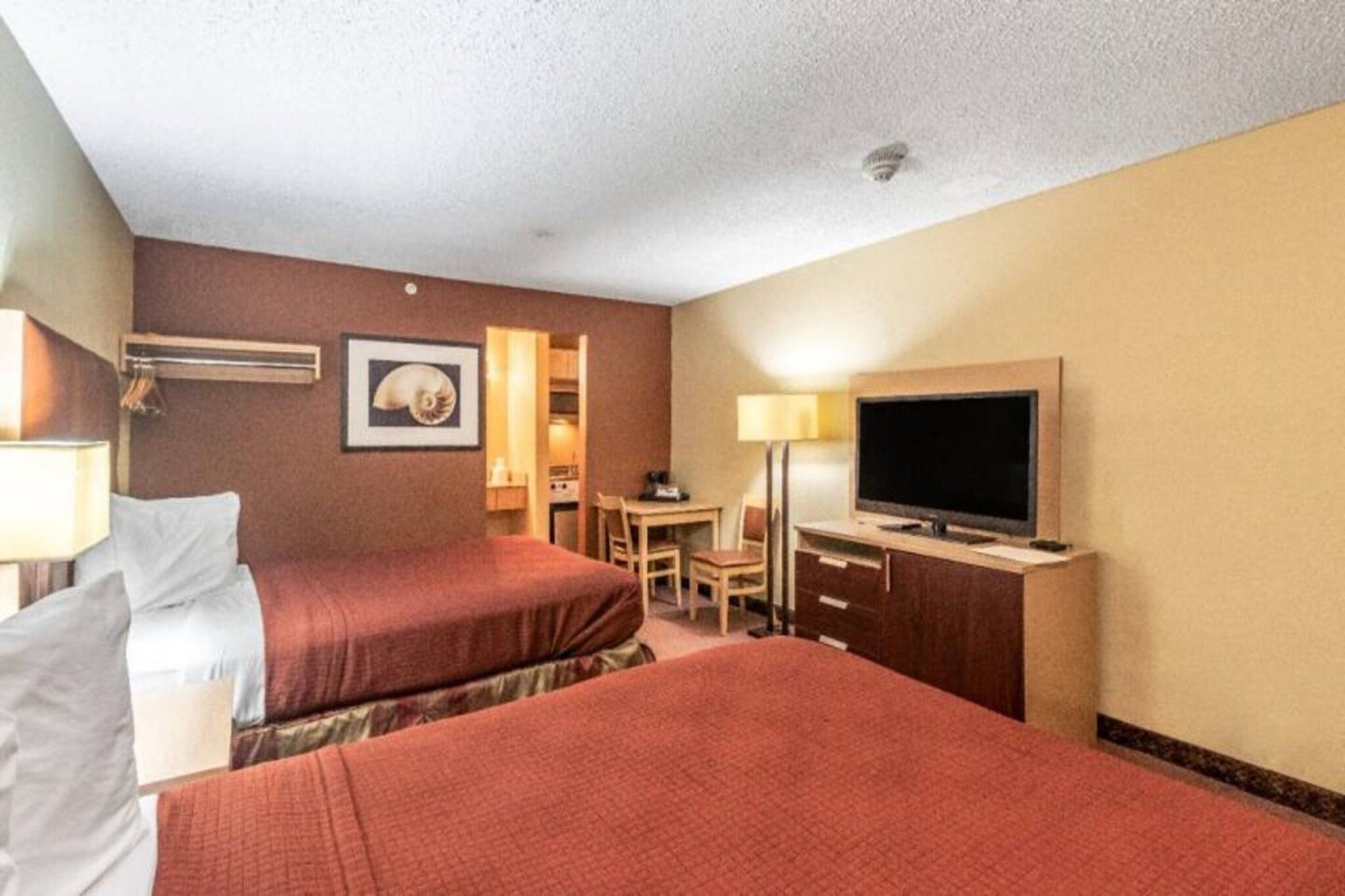 A hotel room with two beds, a desk, a chair, a television, and a framed picture on the wall.