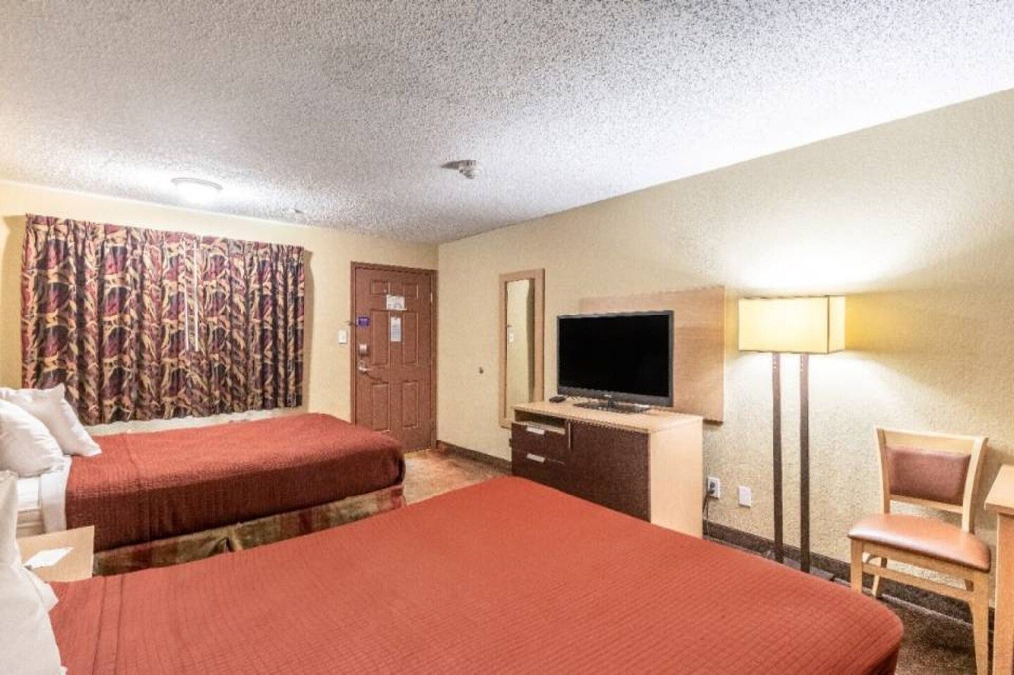 A hotel room with two beds, a desk with a television, a chair, and a lamp.