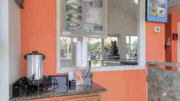 A kitchen with a stove, a pot, and a window with a view of the outside.
