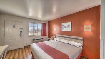 A hotel room with a bed, a desk, a chair, a window with curtains, and a painting on the wall.