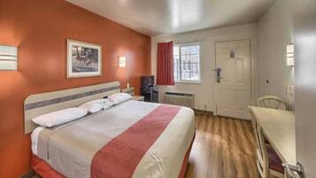 A hotel room with a bed, a desk, a chair, a window, and a door.