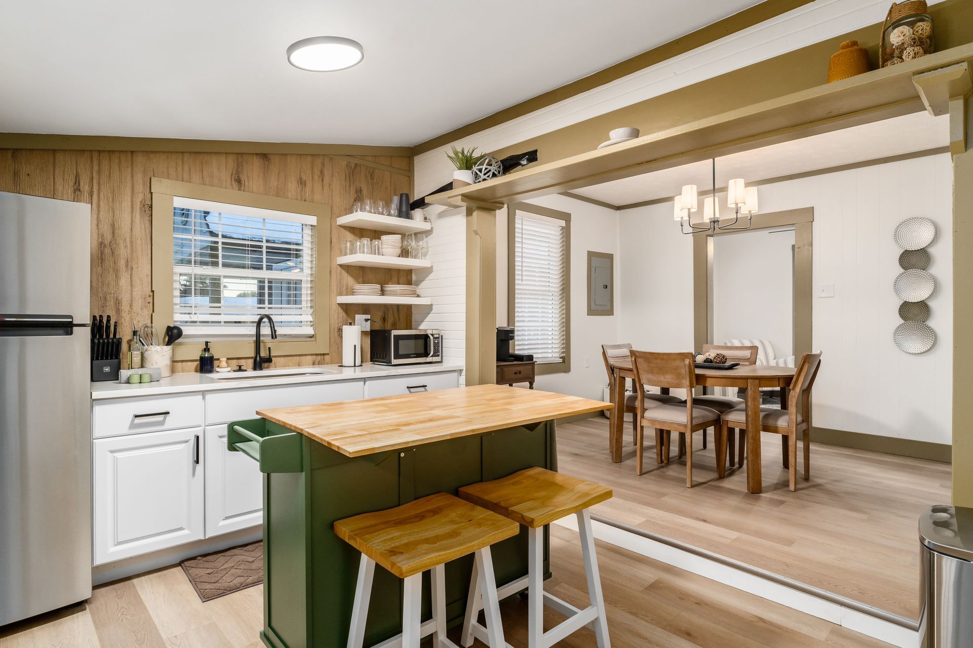 Una cocina moderna con una isla de madera, armarios blancos y un comedor con mesa y sillas de madera.