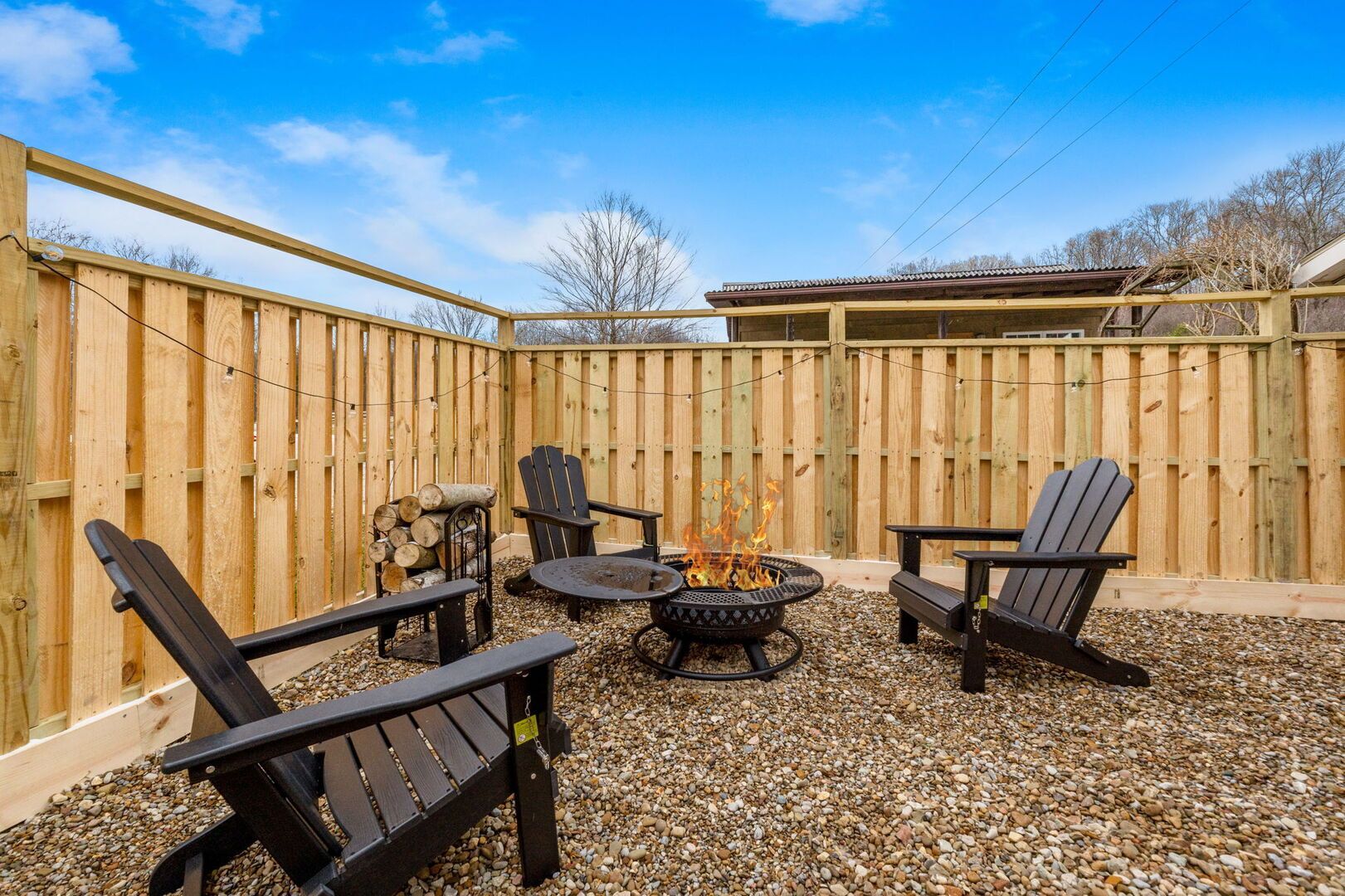 Eine Terrasse im Freien mit Adirondack-Stühlen, einem runden Tisch und einer Feuerstelle.
