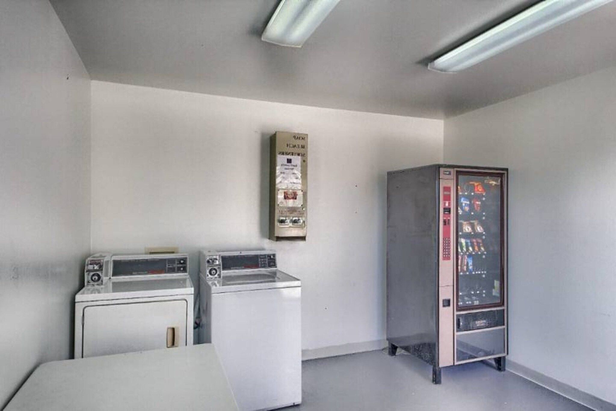 A laundry room with two washing machines and a vending machine.