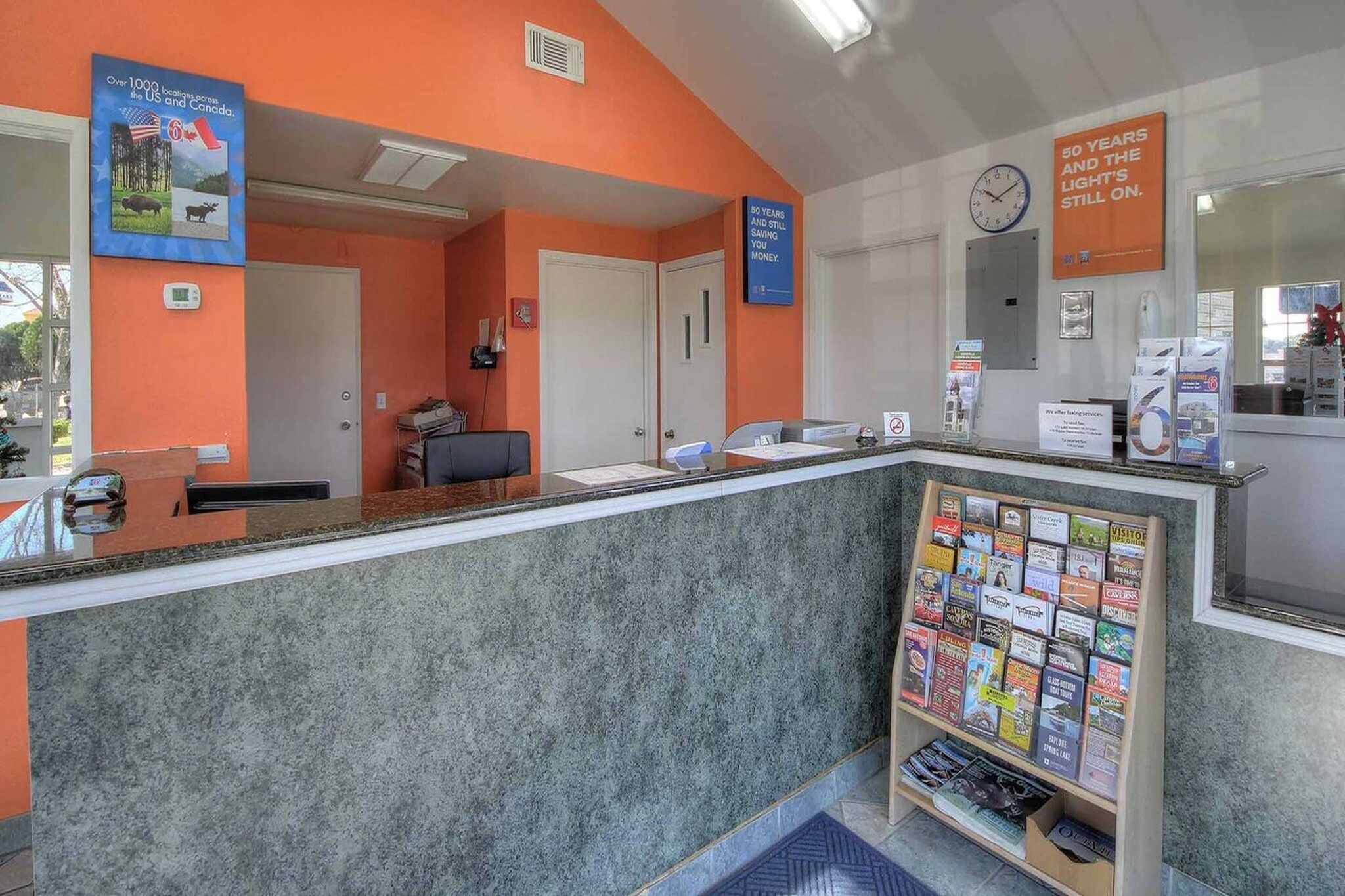 A reception area with a marble counter, a clock, and a bulletin board with travel brochures.