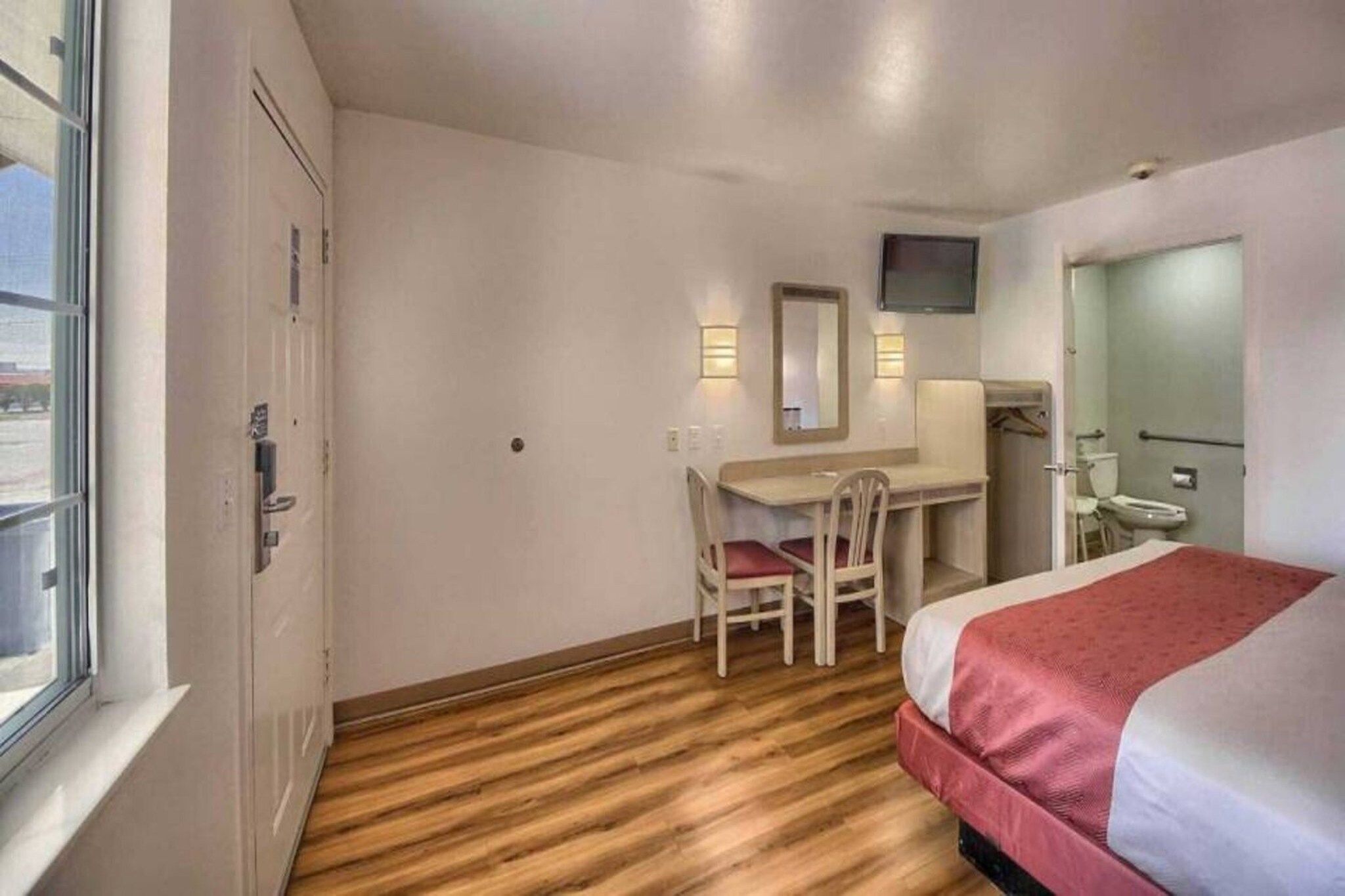 A hotel room with a bed, a desk, a chair, a television, and a window.