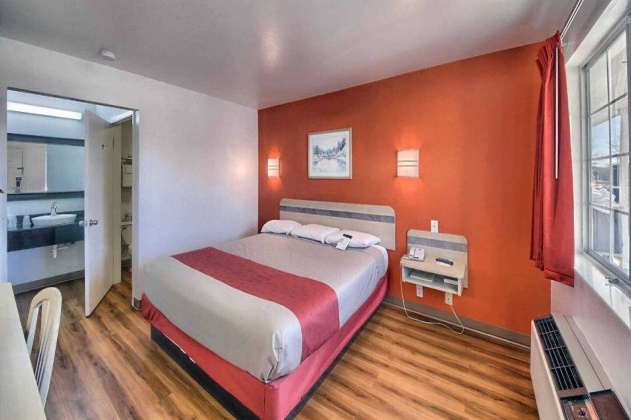 Une chambre d’hôtel avec un lit, une table de chevet, une lampe et une fenêtre avec des rideaux.