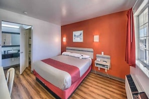Una habitación de hotel con cama, mesita de noche, lámpara y ventana con cortinas.