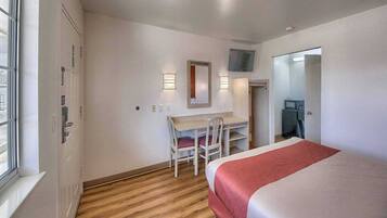 A hotel room with a bed, a desk, two chairs, a mirror, and a television.