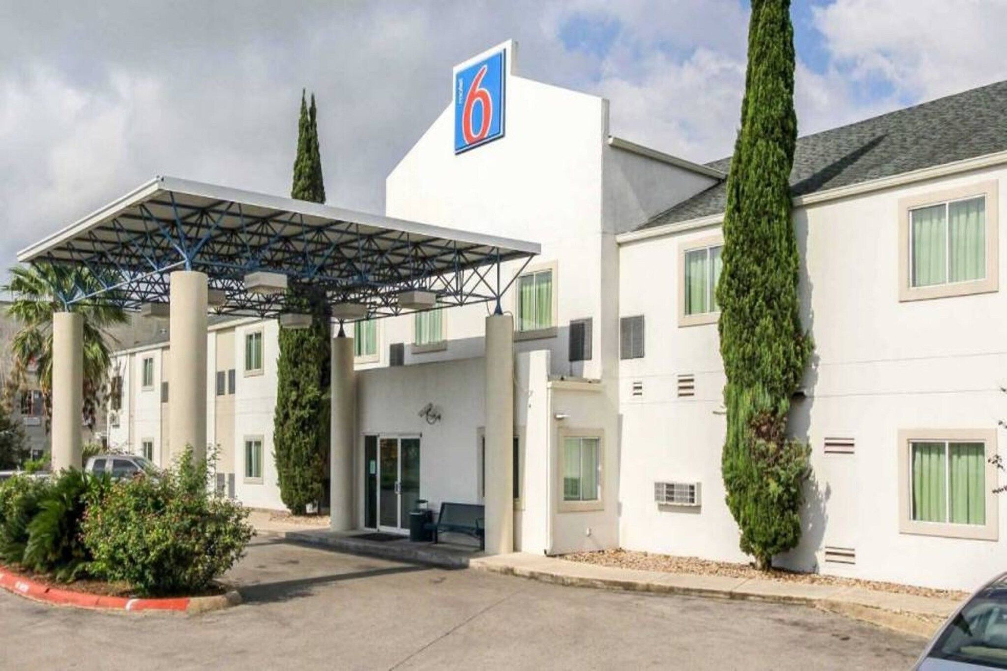 A hotel with a covered entrance, a prominent '6' sign, and tall cypress trees.
