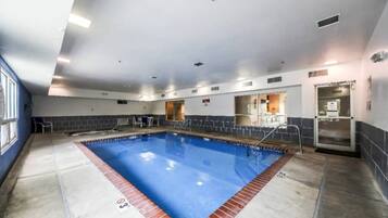 An indoor swimming pool with a clear water surface, surrounded by a tiled deck and a brick border.