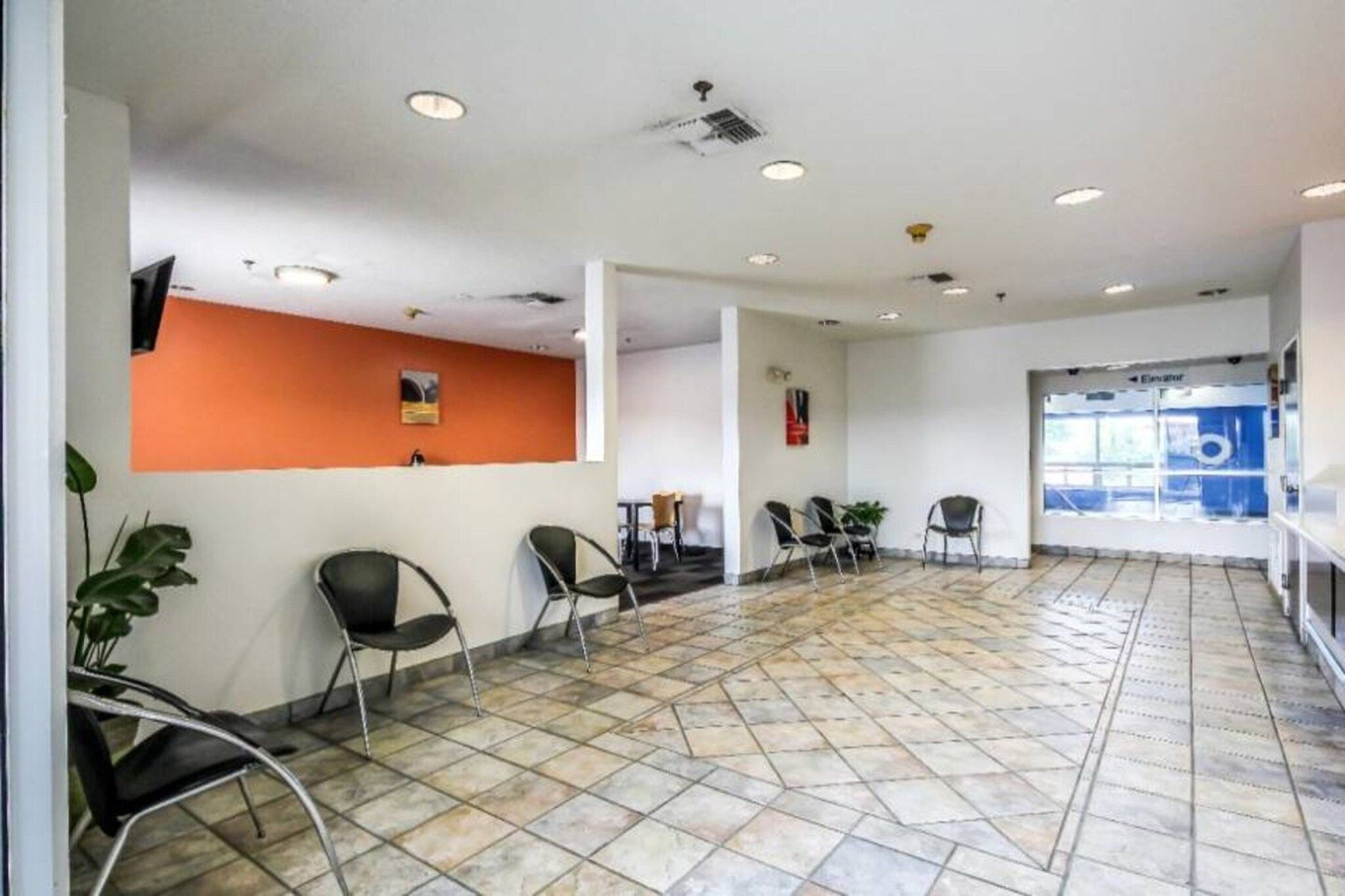 A spacious waiting area with tiled flooring, several chairs, a reception desk, and a visible elevator.