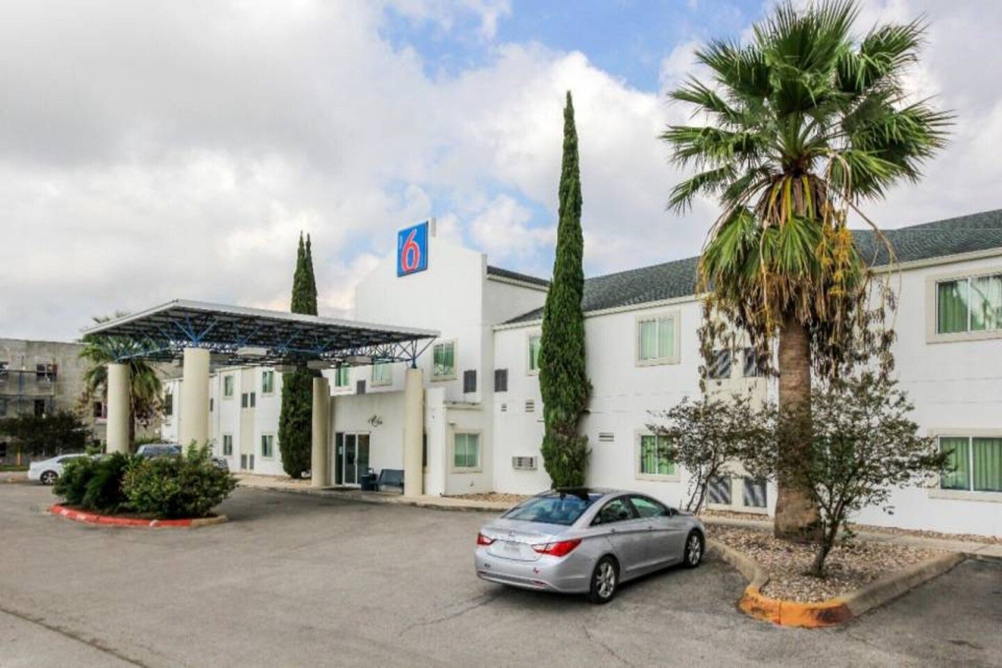 A hotel with a covered parking area, a car parked in front, and a palm tree.