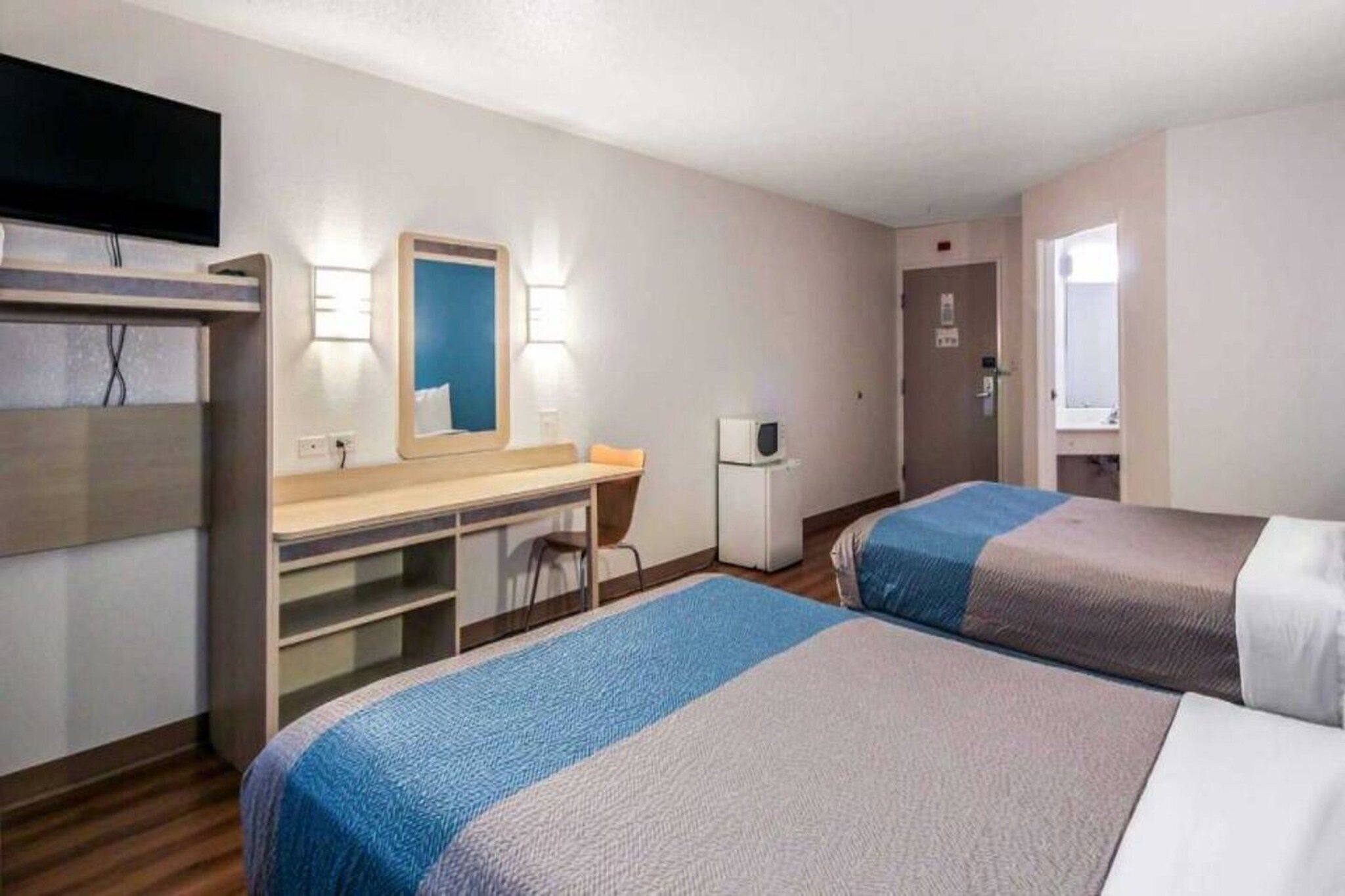 Een hotelkamer met twee bedden, een bureau, een stoel, een televisie en een deur.