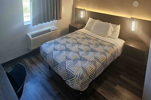 Una habitación de hotel con cama, mesitas de noche, una silla, un calentador y una ventana con cortinas.