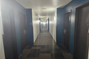 Un pasillo de hotel con puertas a ambos lados, piso a cuadros y un plafón con lámpara.