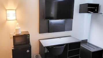 Habitación compacta con televisión de pantalla plana montada en la pared, un escritorio pequeño con una silla, un cesto de basura y un mueble de almacenamiento compacto.