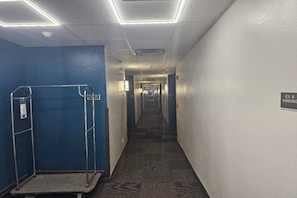 A hotel corridor with a blue wall on one side, a metal rack, and a sign indicating an ice and vending area.