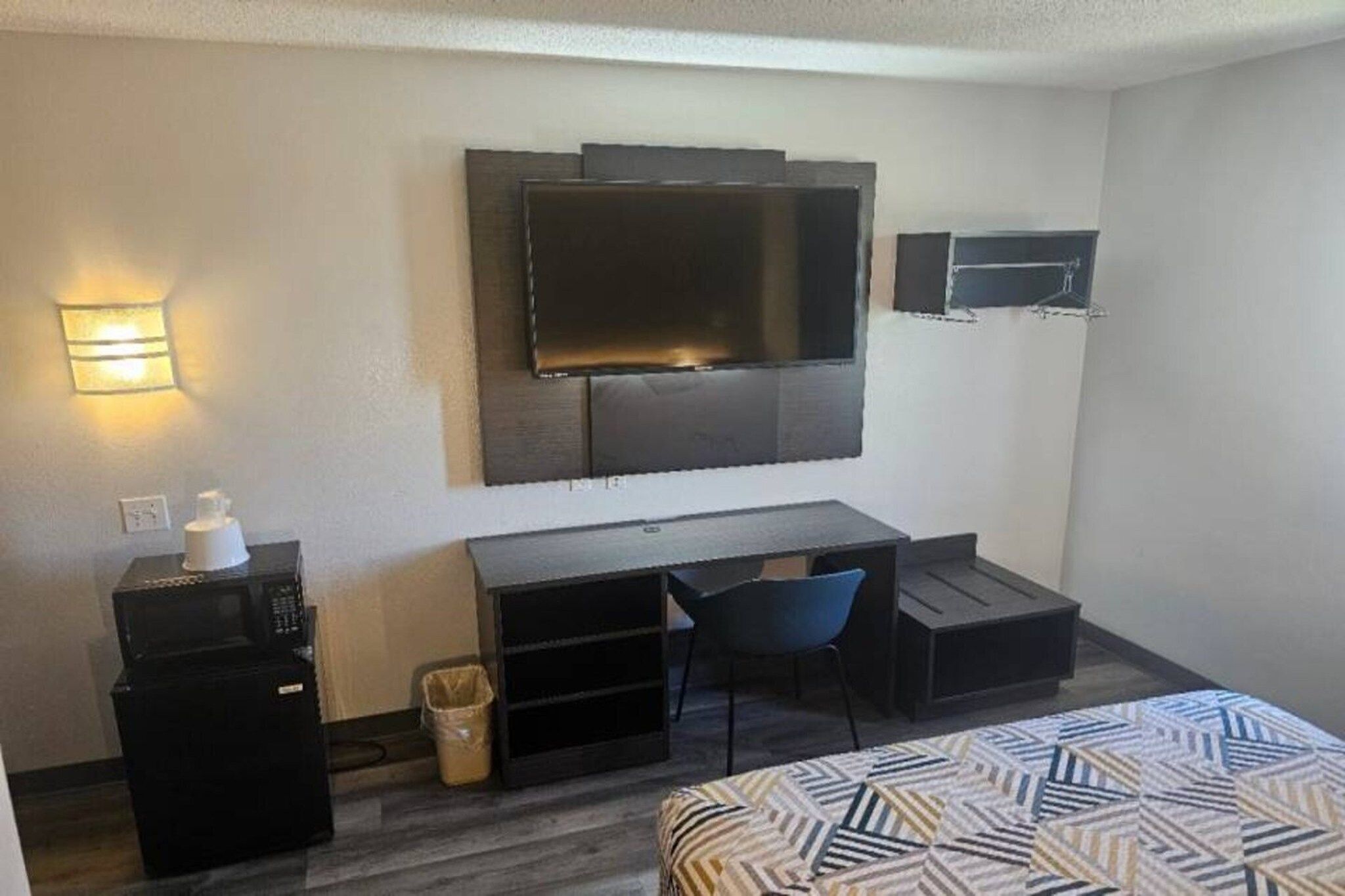 Una habitación de hotel con cama, escritorio, silla, televisor y basurero.