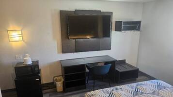 Una habitación de hotel con cama, escritorio, silla, televisor y basurero.