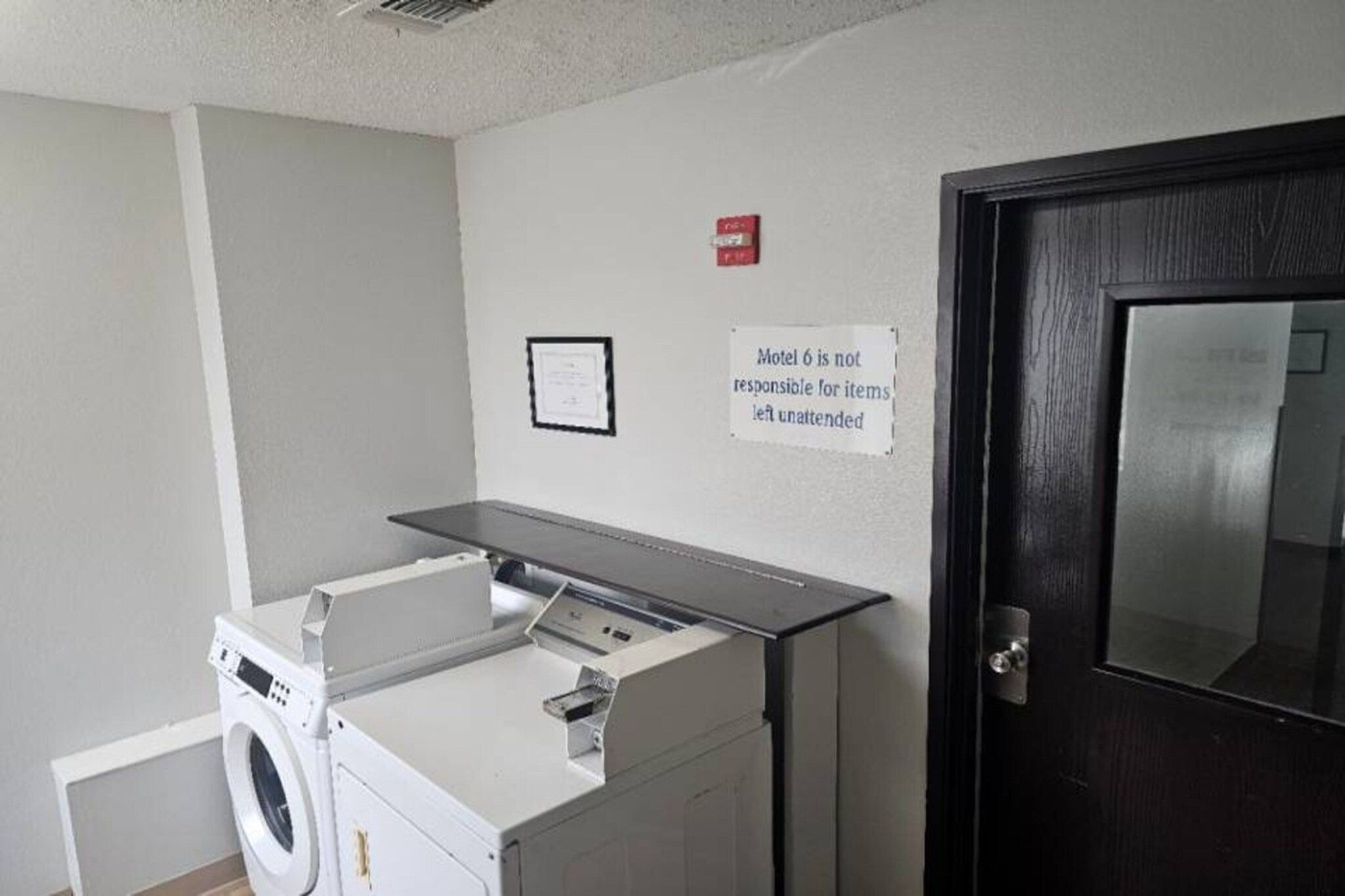 A laundry room with a washing machine, dryer, and a sign stating 'Motel 6 is not responsible for items left unattended.'
