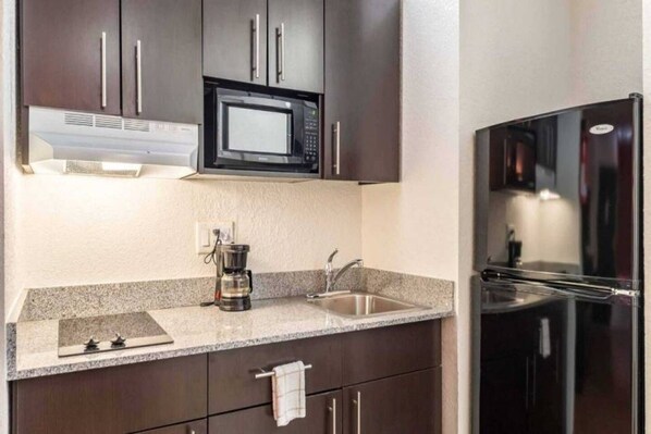 A modern kitchen with dark cabinets, a microwave, a coffee maker, and a refrigerator.