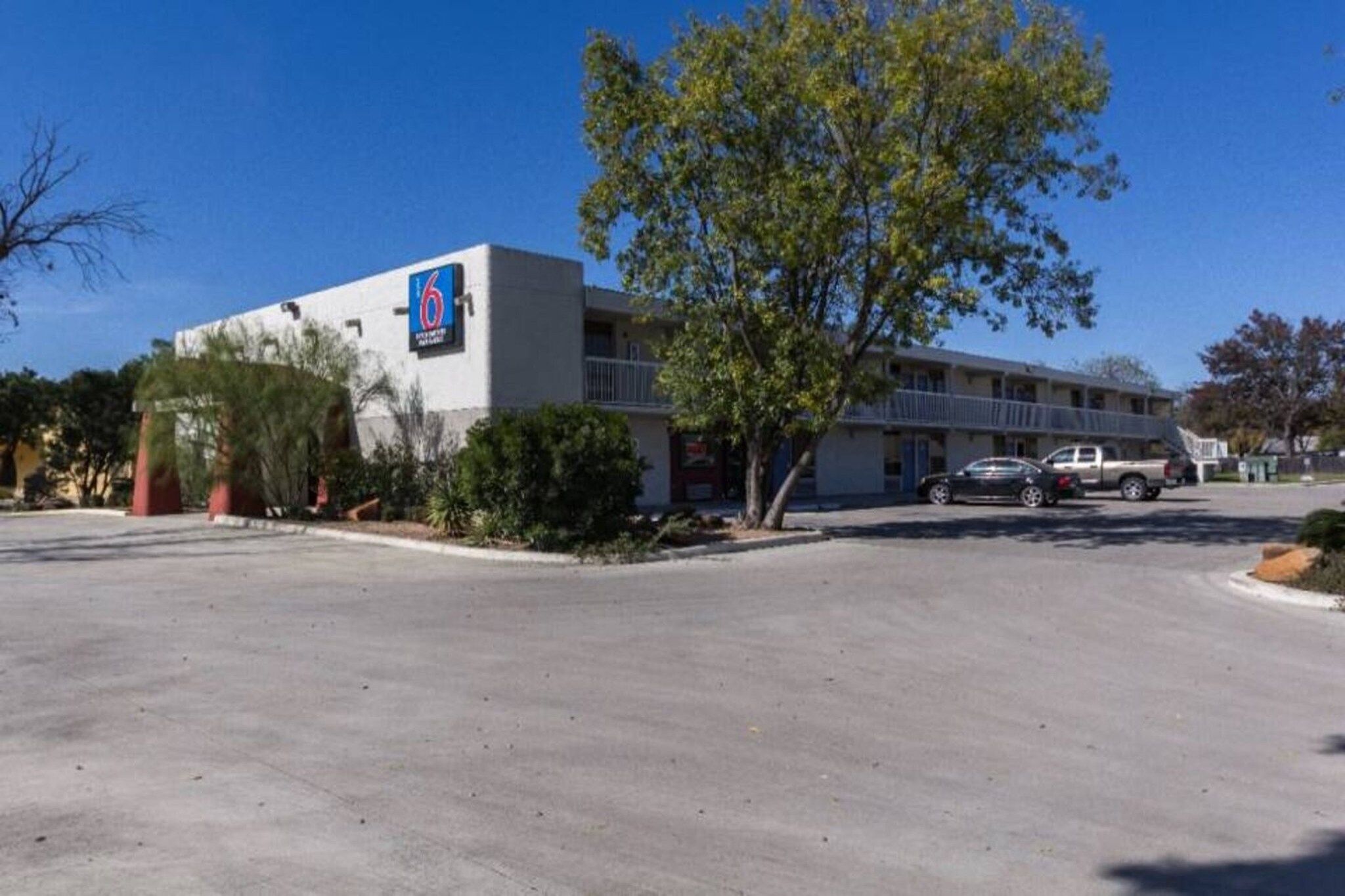 A motel with a large sign, a parking lot, and a tree in front.