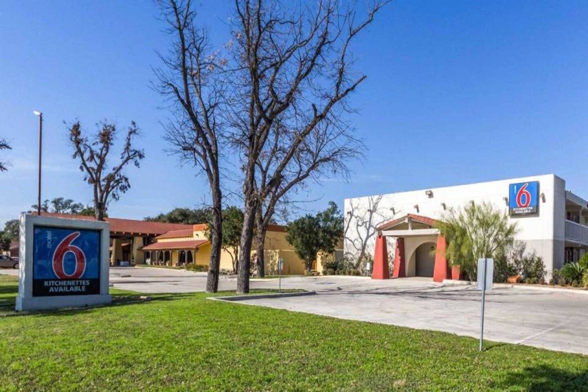 A 6 Kitchenettes available motel with a parking lot, a building entrance, and a clear sky.