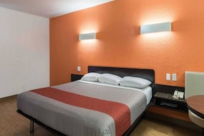 Een hotelkamer met een bed, nachtkastje, stoel en een wandlamp.