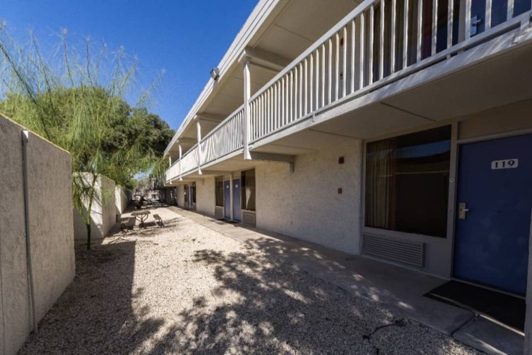 A row of motel rooms with a covered walkway and a blue door marked with the number 119.