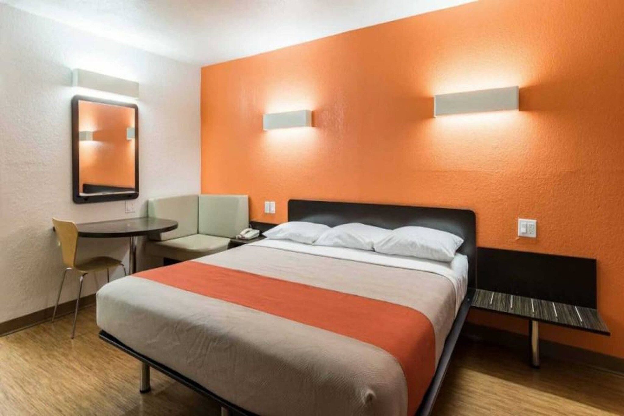 A hotel room with a bed, a desk, a chair, and a mirror.